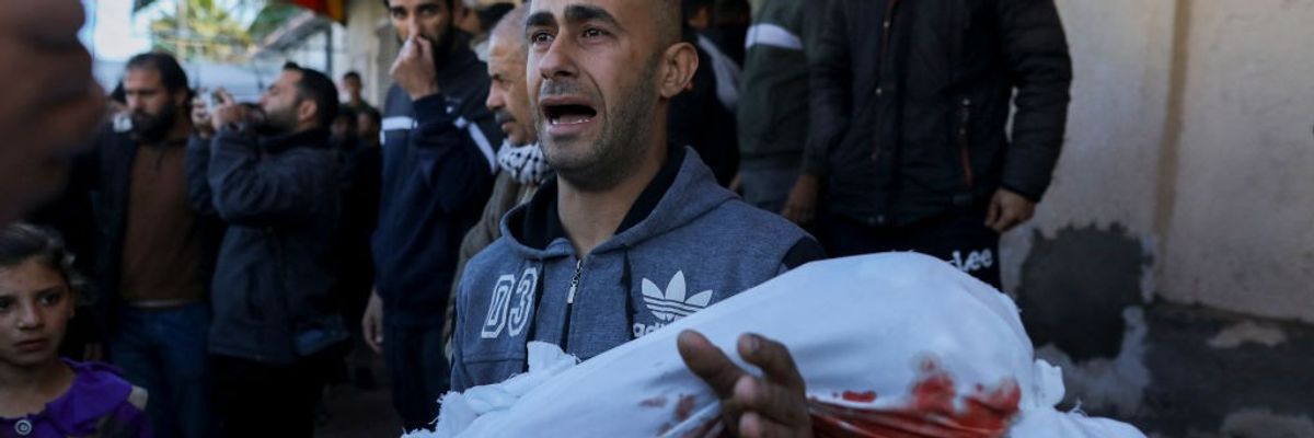 A father cries while carrying the body of his child wrapped in a blood-stained shroud