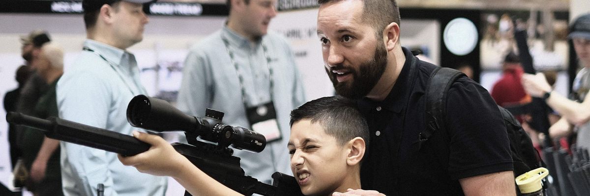 A father helps his son try out a gun at the National Rifle Association Convention