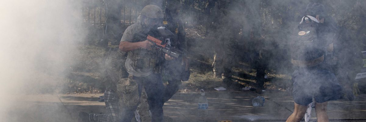 A federal law enforcement agent fires pepper balls at a woman while tear gas fills the air
