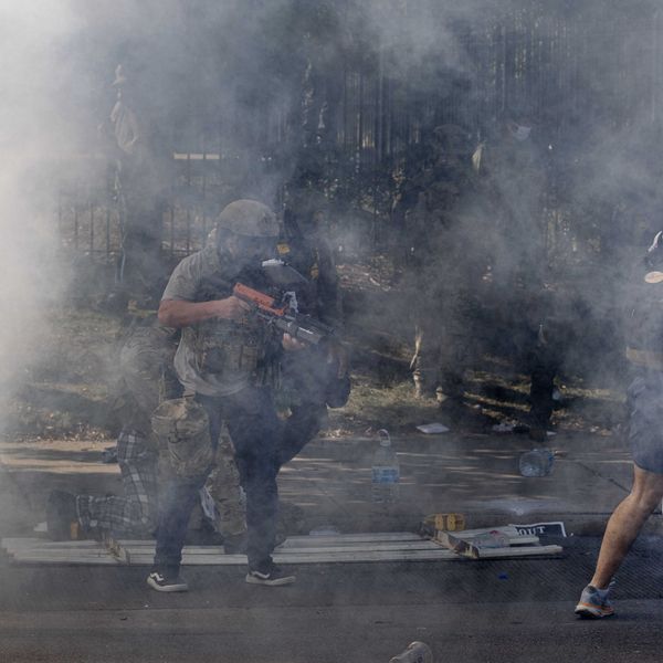 A federal law enforcement agent fires pepper balls at a woman while tear gas fills the air