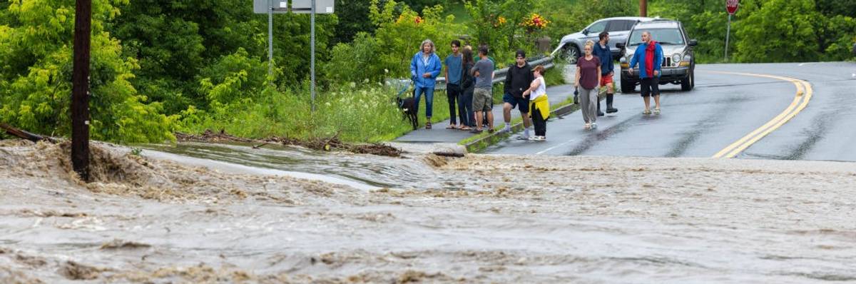 A flood crosses a roadway blocking a crowd who stand outside their vehicle.