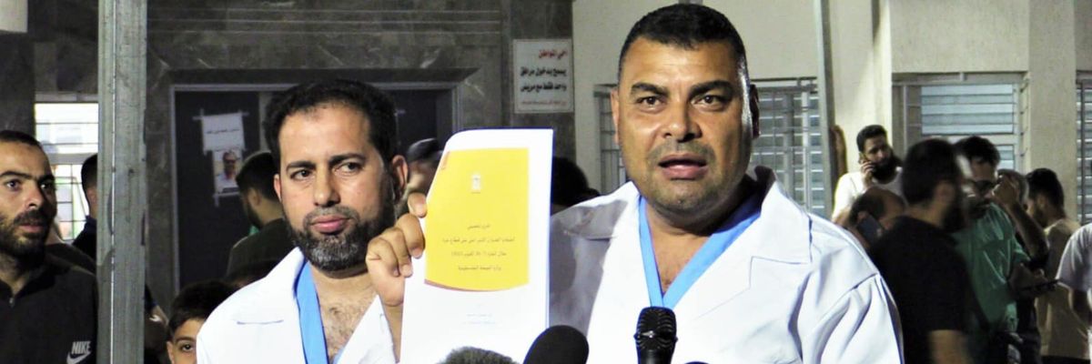 A Gaza health official in a white medical coat holds a list of the 6,747 people killed by Israeli bombing and shelling. 