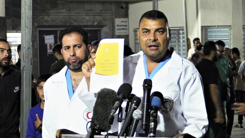 A Gaza health official in a white medical coat holds a list of the 6,747 people killed by Israeli bombing and shelling.