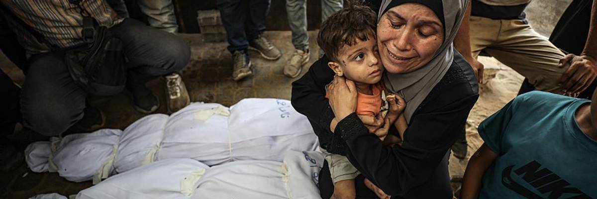 A Gaza woman holds a child and weeps over wrapped bodies