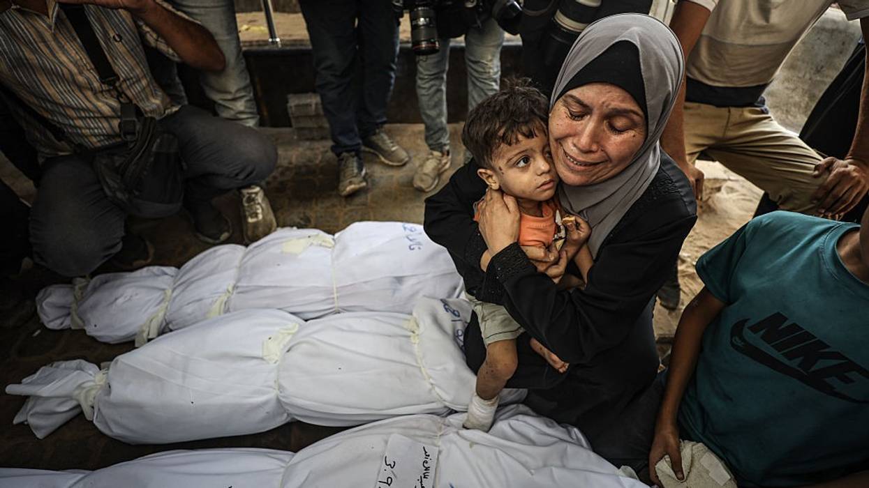A Gaza woman holds a child and weeps over wrapped bodies