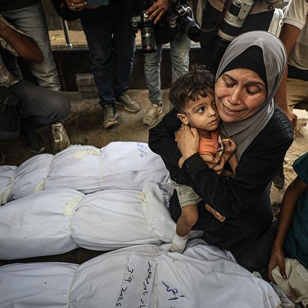 A Gaza woman holds a child and weeps over wrapped bodies