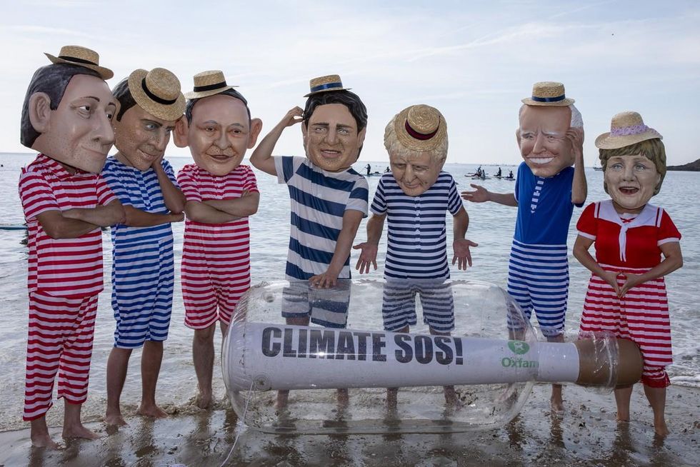 A giant message in a bottle has washed up on the beach from countries ravaged by climate change, but the G7 leaders are too busy relaxing in their swimming costumes in deck chairs to notice, Oxfam campaigners pose as G7 leaders on a beach on the 12th of June 2021 near Falmouth, Cornwall, United Kingdom.