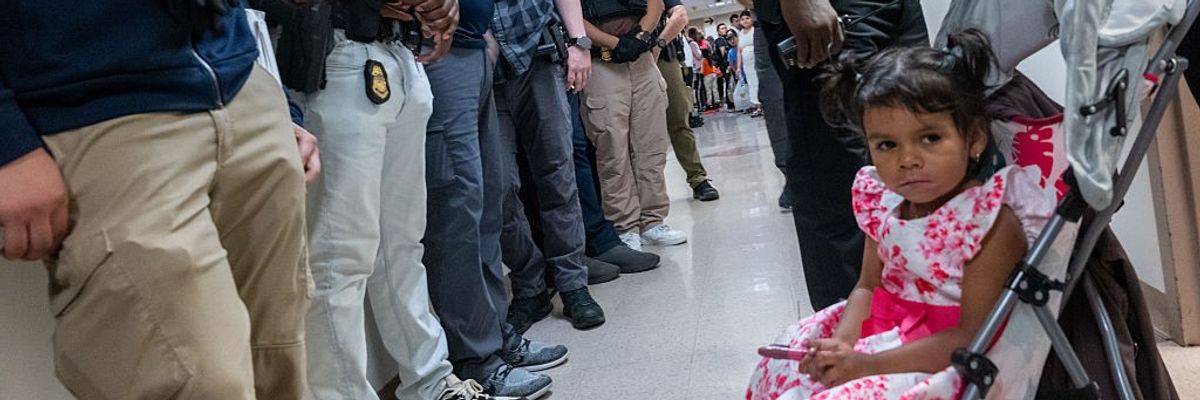 A girl in a stroller sits in front of a line of masked federal agents in immigration court