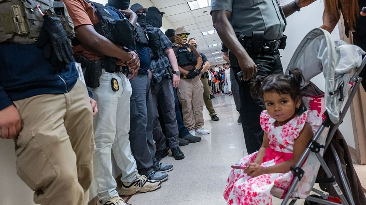 A girl in a stroller sits in front of a line of masked federal agents in immigration court