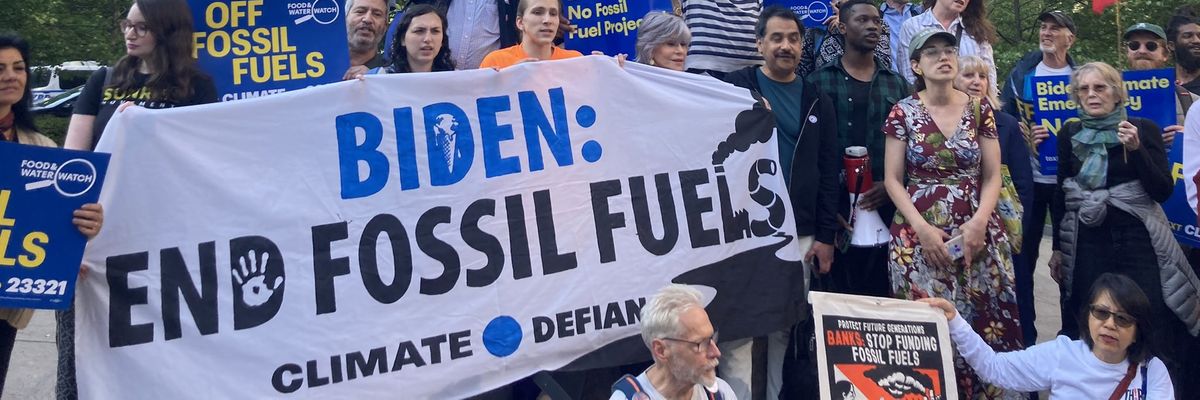 A group of people gathers behind a banner reading, "Biden: End Fossil Fuels."