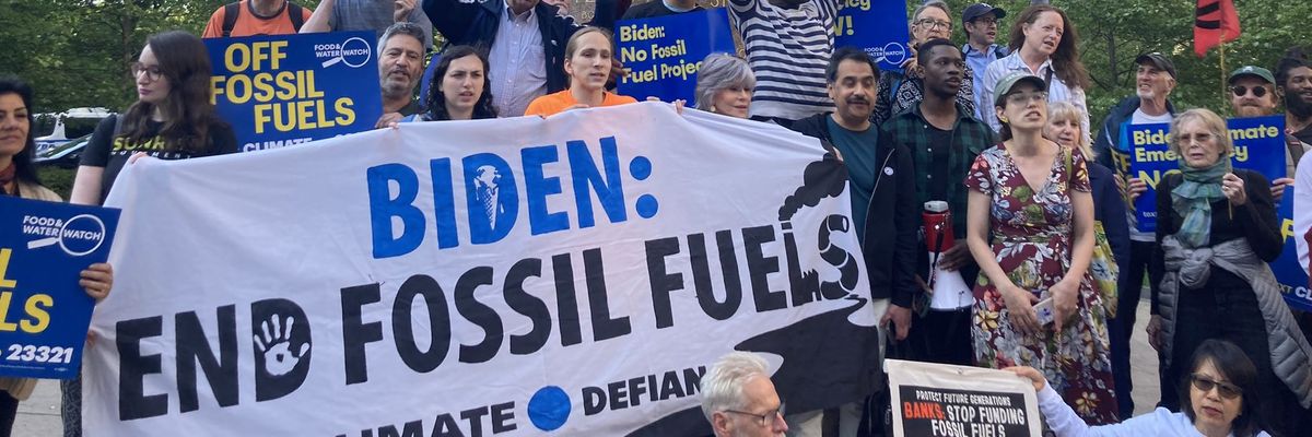 A group of people gathers behind a banner reading, "Biden: End Fossil Fuels."