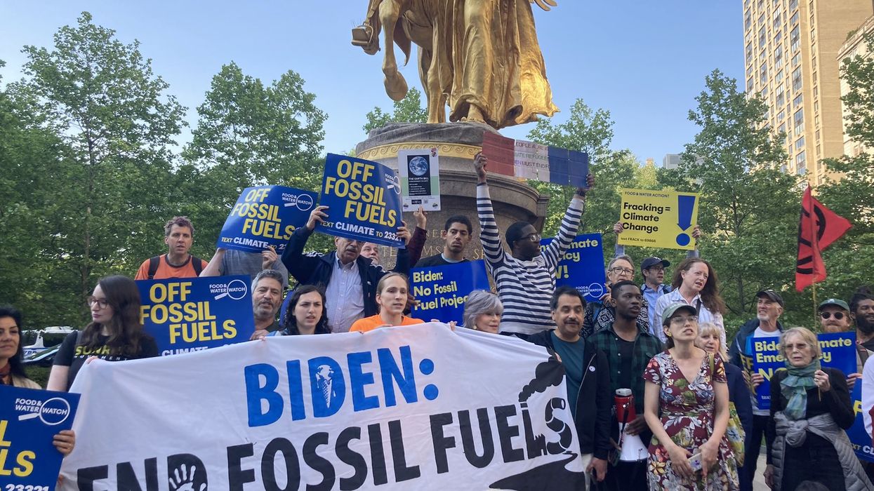 A group of people gathers behind a banner reading, "Biden: End Fossil Fuels."