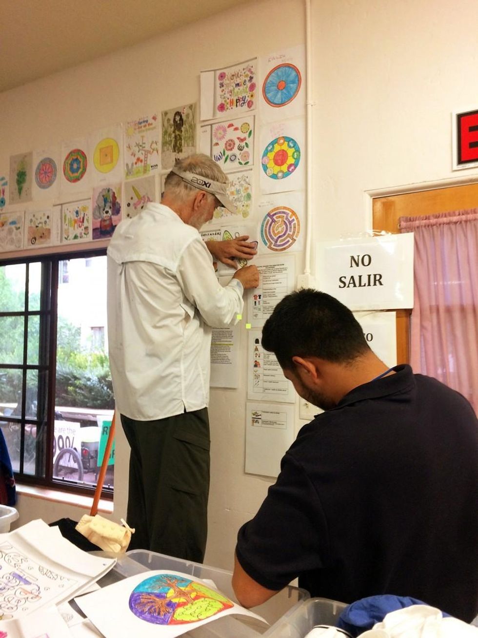A guest and a local volunteer work to curate a wall of children's drawings in the clothing room. (Photo: Rose Lambert-Sluder)