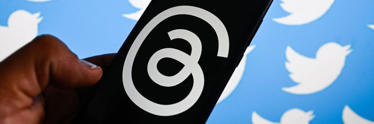 A hand holds a black phone covered with the white Threads logo against a background of Twitter birds.