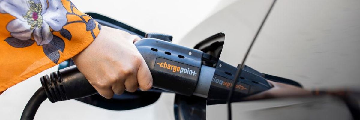 A hand in an orange sleeve charges an electric vehicle. 