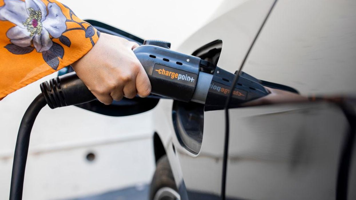 A hand in an orange sleeve charges an electric vehicle.