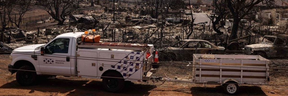 A Hawaiian Electric truck park next to a burnt neighborhood in Maui.