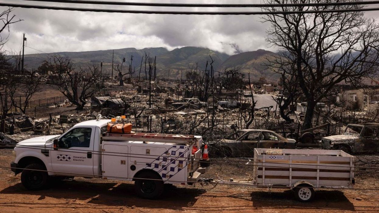A Hawaiian Electric truck park next to a burnt neighborhood in Maui.