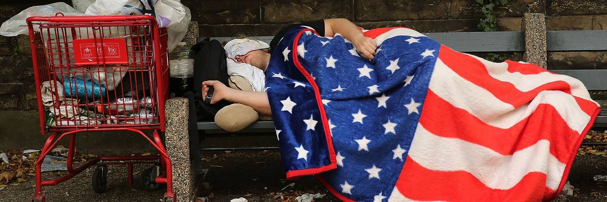 A homeless person sleeps under a US flag.