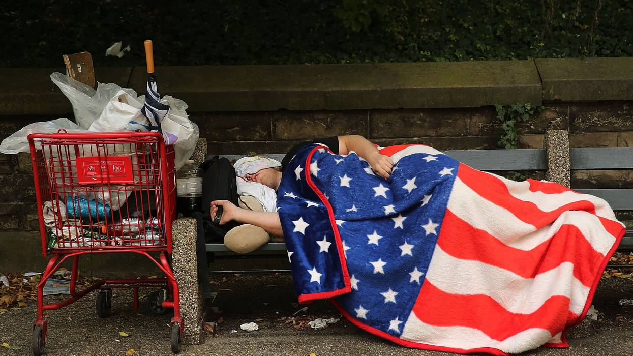 A homeless person sleeps under a US flag.