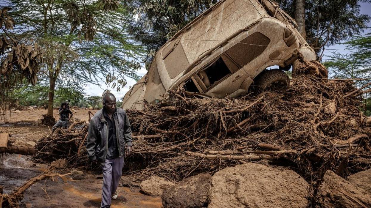 a Kenyan man walks by an SUV tossed about by floodwaters
