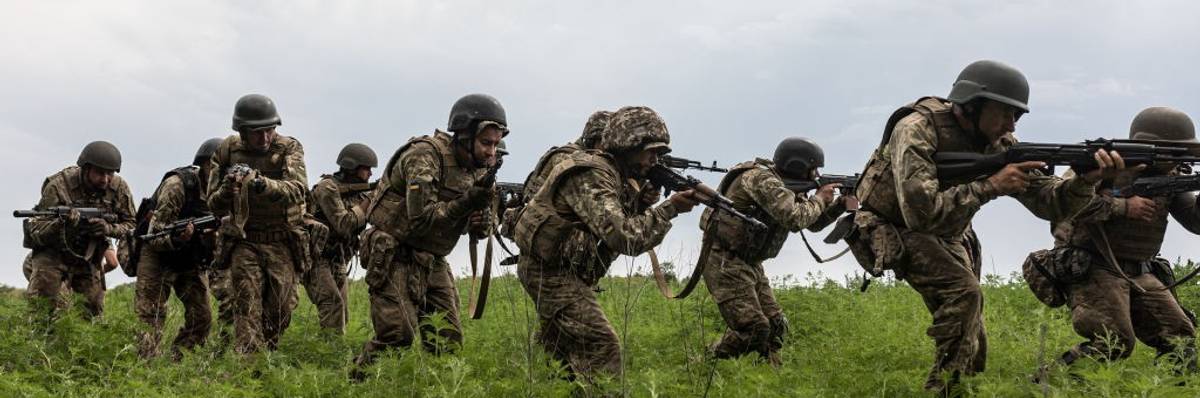 A line of Ukrainian soldiers crouches in line in a field with guns.