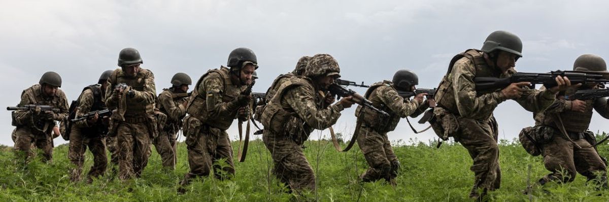 A line of Ukrainian soldiers crouches in line in a field with guns.