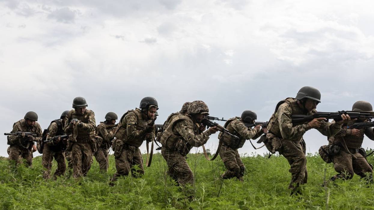 A line of Ukrainian soldiers crouches in line in a field with guns.