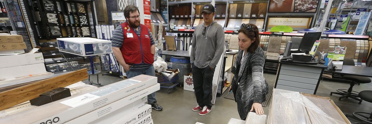 A Lowe's employee helps two customers look at flooring.