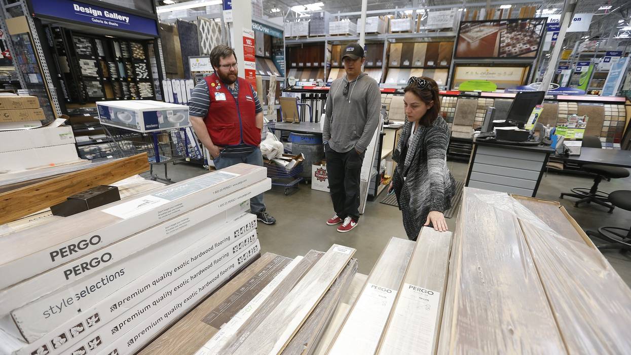 A Lowe's employee helps two customers look at flooring.