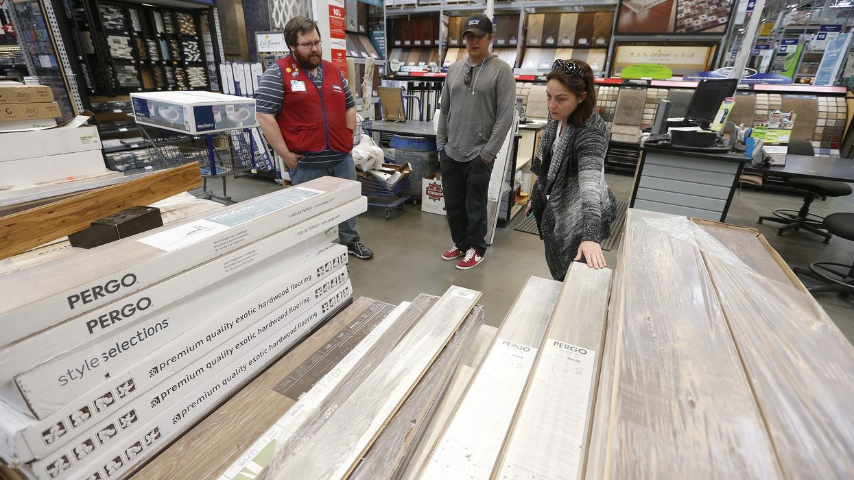 A Lowe's employee helps two customers look at flooring.