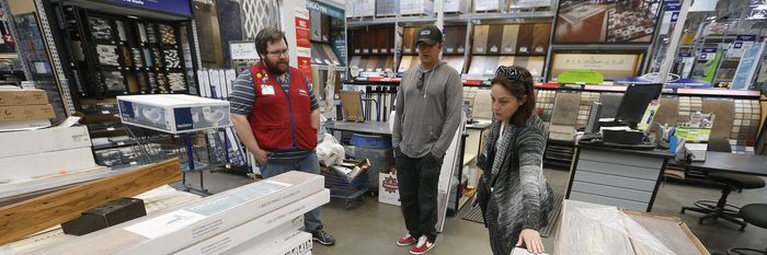 A Lowe's employee helps two customers look at flooring.
