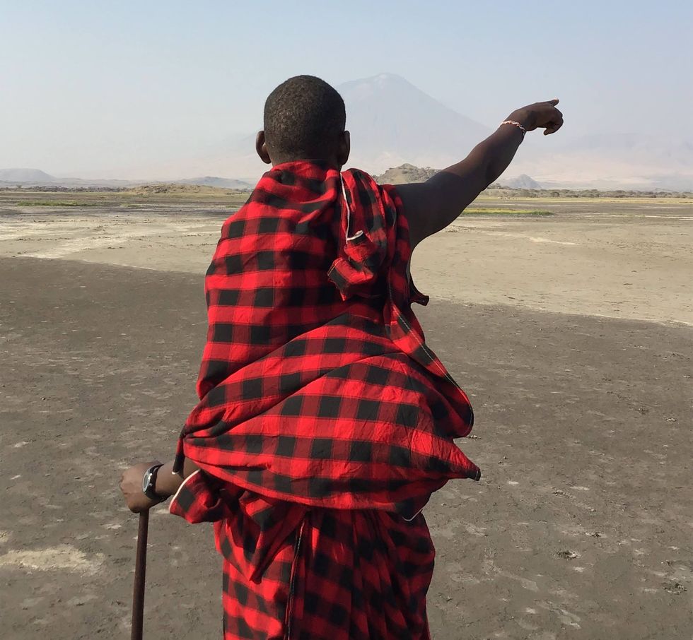 A Maasai individual in a red-and-black checkered cloak points into the distance.