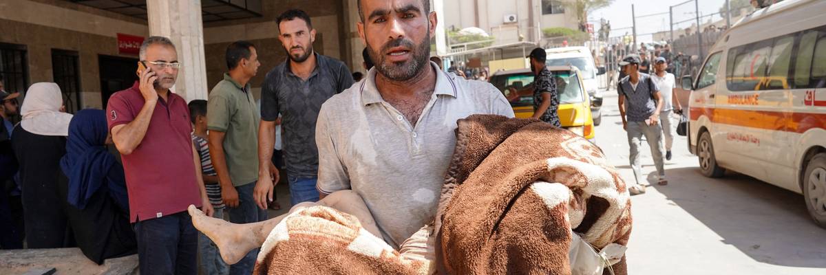 A man carries a child wrapped in a blanket at Nasser Hospital