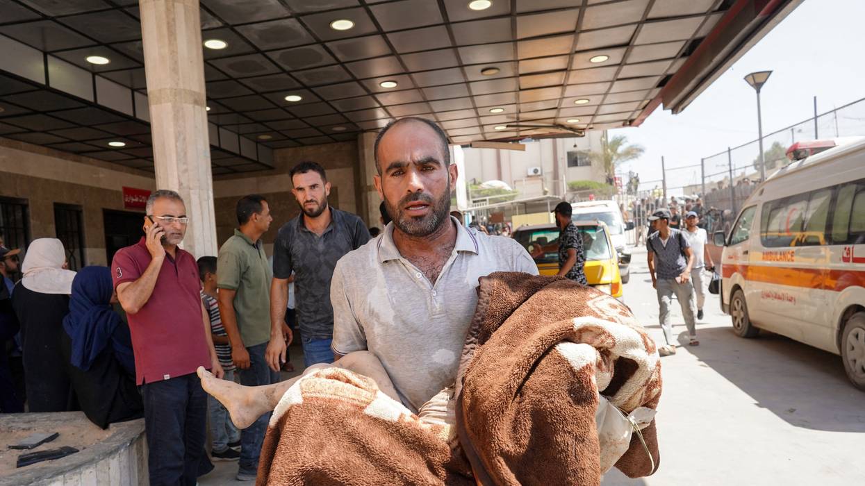 A man carries a child wrapped in a blanket at Nasser Hospital