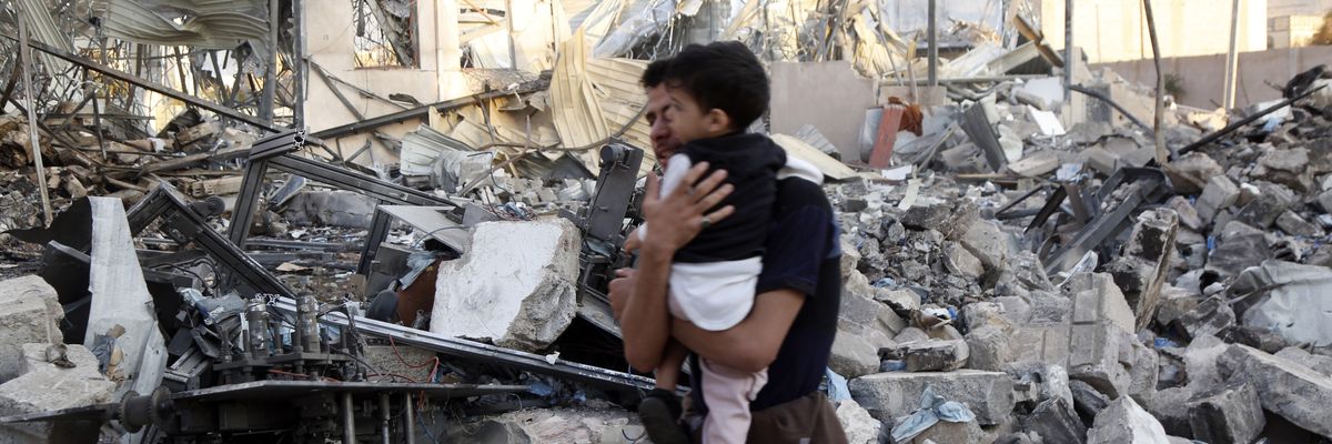 A man carries his child near the rubble of a building targeted by the United States' aerial attacks