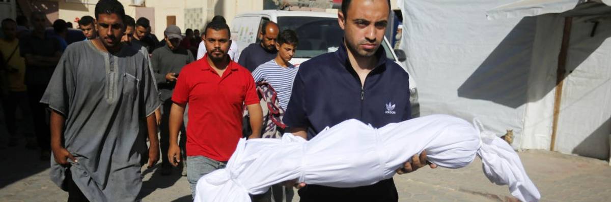 A man carries the body of a Palestinian child wrapped in a white sheet.