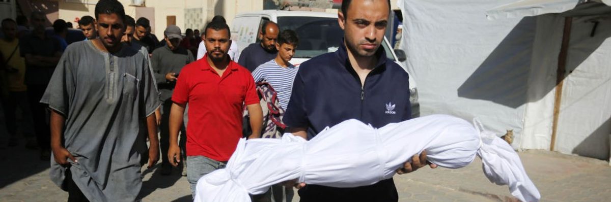 A man carries the body of a Palestinian child wrapped in a white sheet.