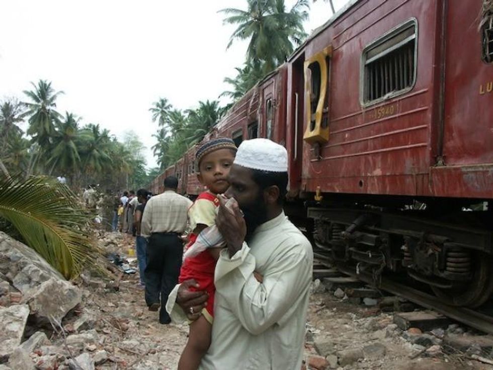 A man covers his nose and mouth with a handkerchief to shield himself from the smell emanating from the train, as dead bodies decompose in the sun. (Photo: Amantha Perera/IPS)