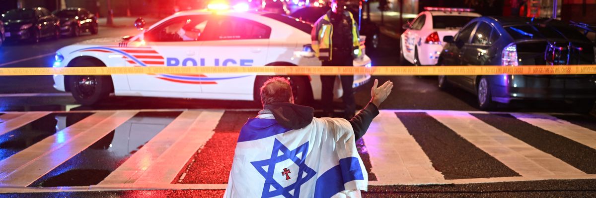 A man draped in an Israeli flag gestures at the crime scene where two Israeli diplomats were shot in D.C.
