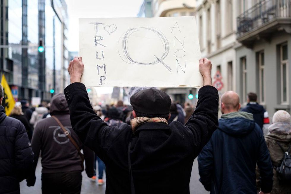 A man holds a placard with 'Trump loves QAnon'