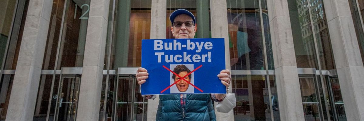 A man holds a sign reading, "Buh-bye Tucker!"