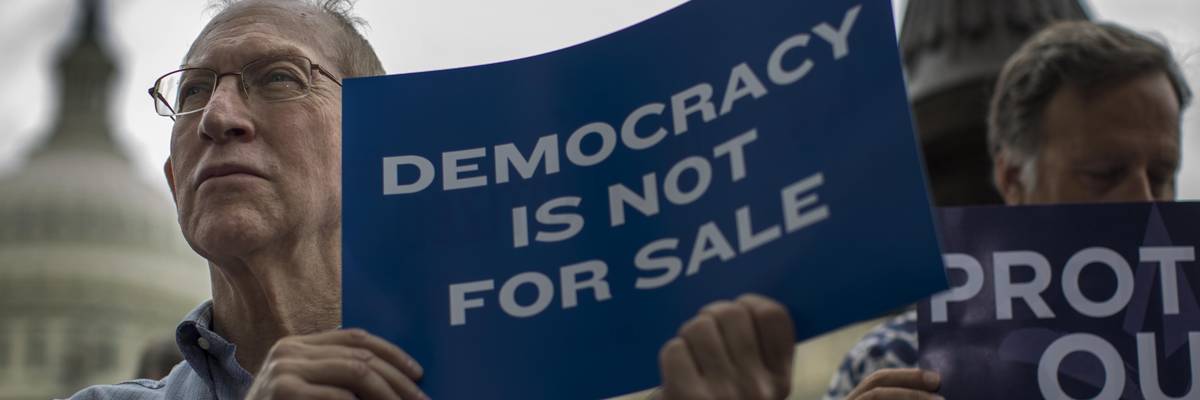 A man holds a sign reading, "Democracy is not for sale."