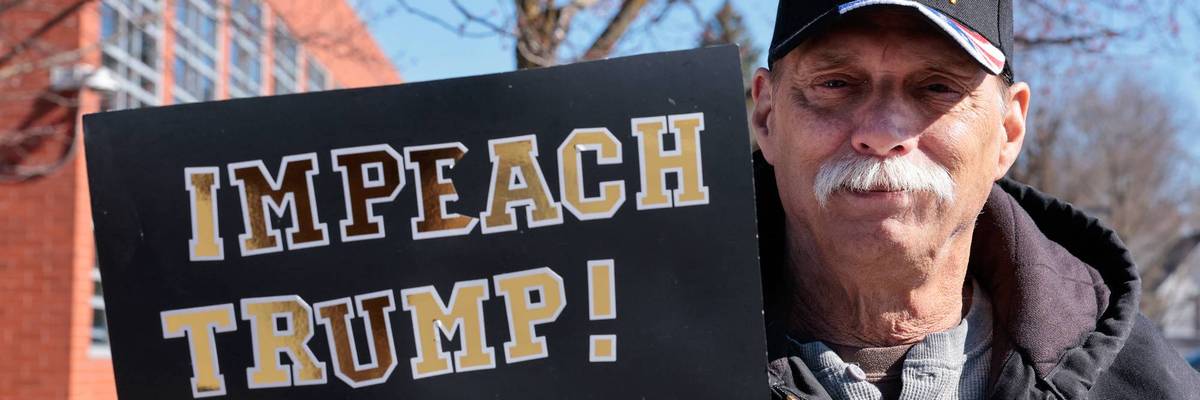 A man holds a sign reading "Impeach Trump"