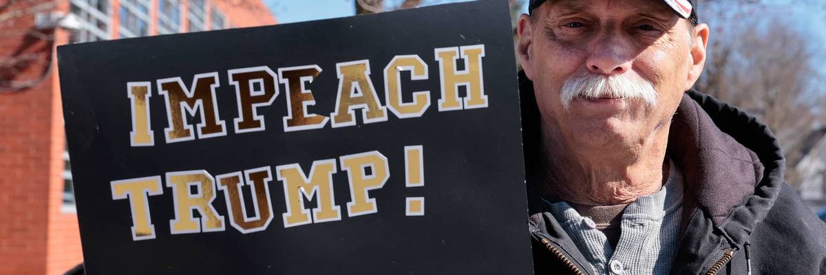 A man holds a sign reading, "Impeach Trump."