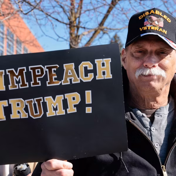 A man holds a sign reading "Impeach Trump"