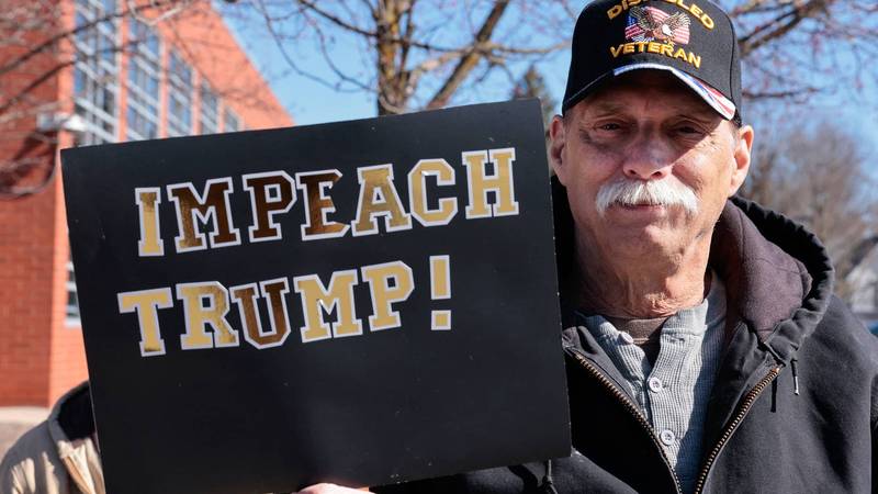 A man holds a sign reading "Impeach Trump"