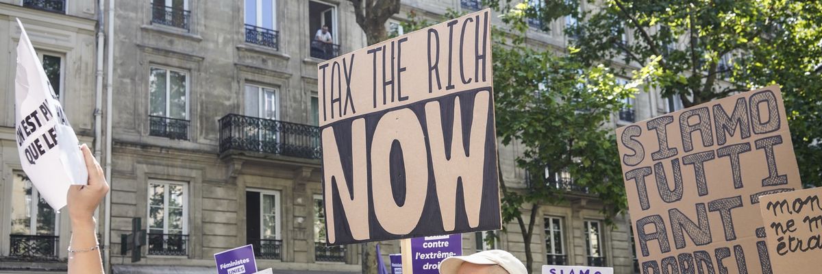 A man holds a sign reading, "Tax the Rich Now"