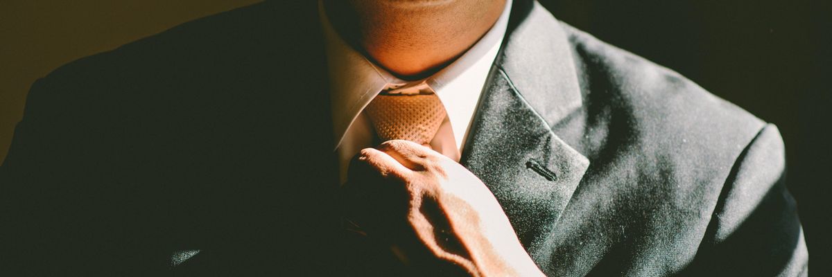 A man in a black suit loosening his tie