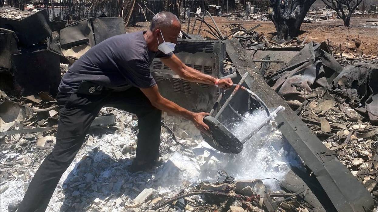A man in a face mask removes items from the ashes of his home.